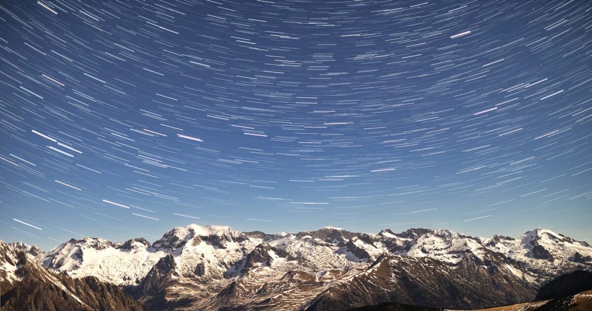 A view of a mountain range with a star trail in the sky