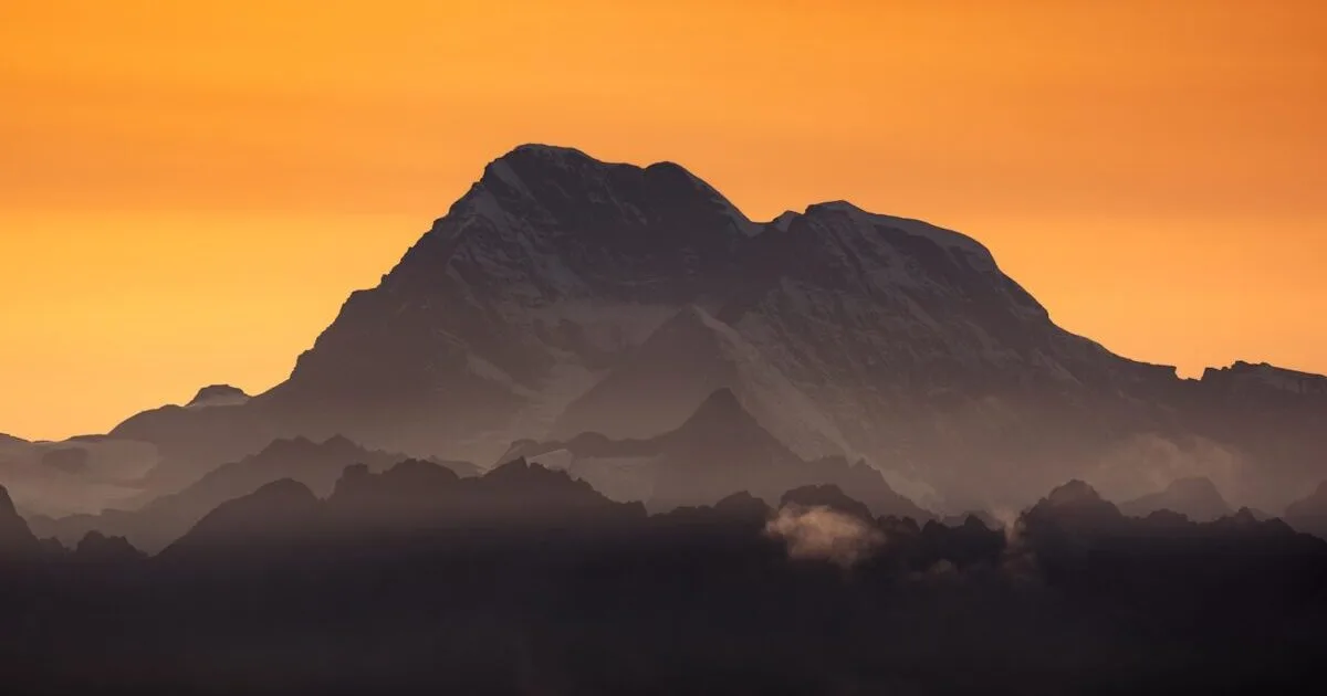 Majestic mountain silhouetted against an orange sky.